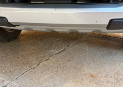 Front bumper of a Ford vehicle with partial license plate text visible, parked on cracked concrete ground.
