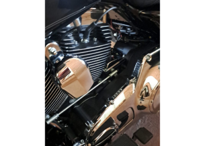 Close-up of a V-twin motorcycle engine with chrome covers and black cooling fins on a dark bike surface.